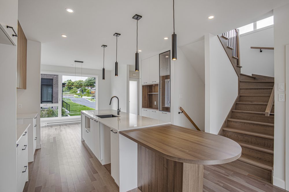 Aire ouverte d'une maison neuve : îlot de cuisine avec comptoir de quartz, table en bois et escalier