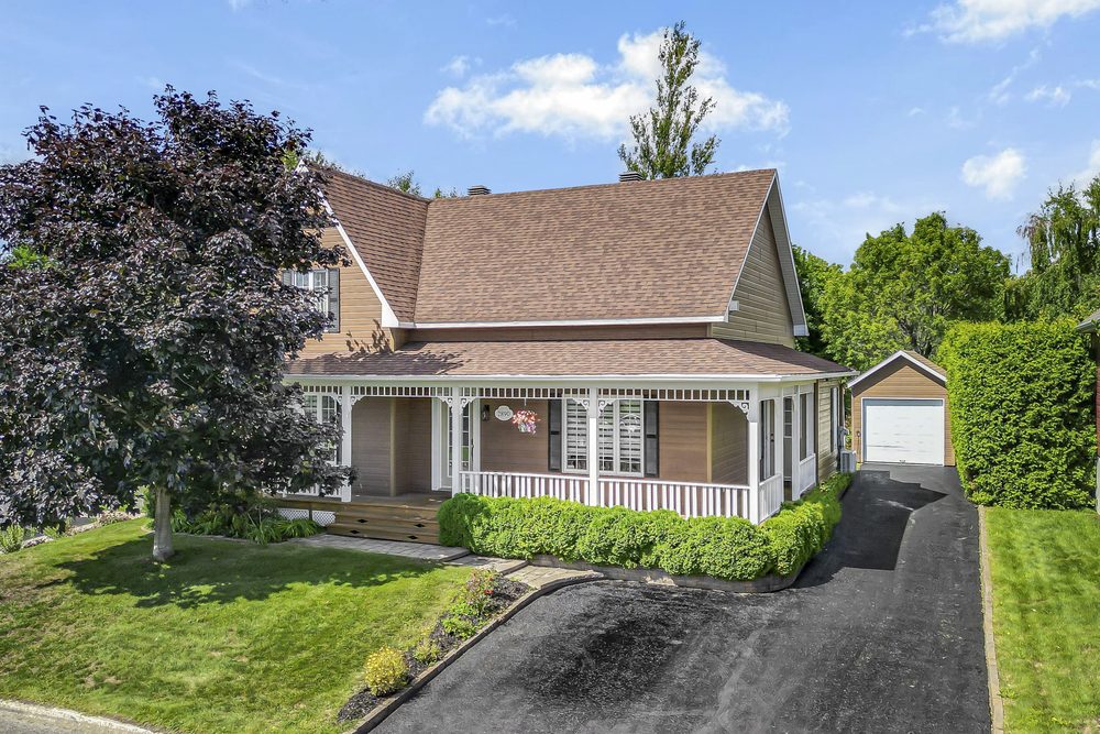 Façade d'une maison avec galerie couverte, aménagement paysager et garage détaché