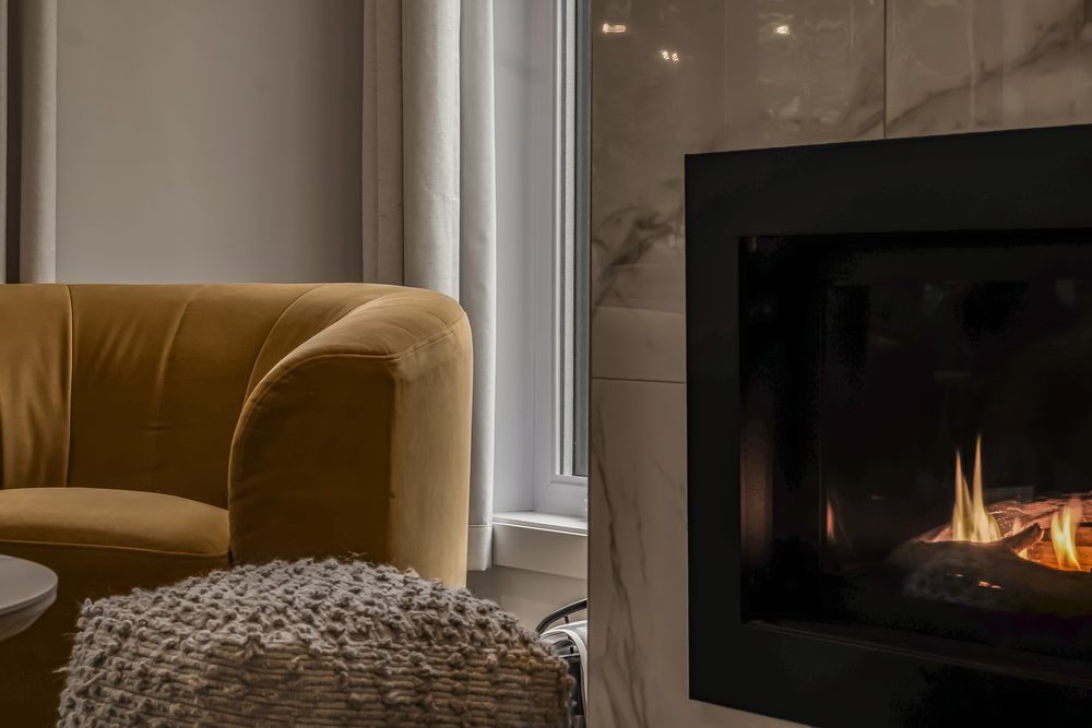 Fauteuil moutarde et pouf tricoté près du foyer allumé, en fin de journée
