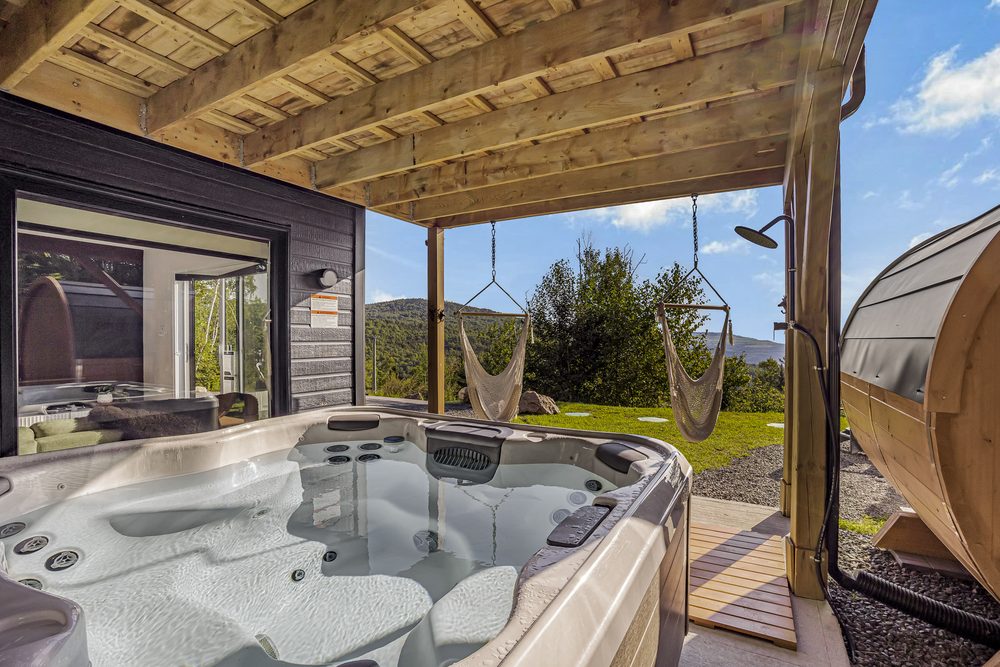 Spa extérieur sous une pergola avec sauna, chaises suspendues et vue sur les montagnes